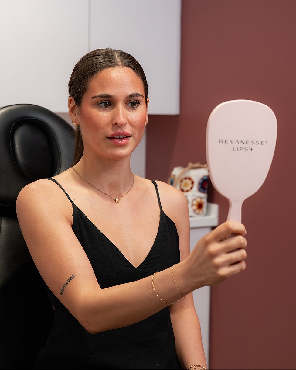 Woman examining lips in mirror at clinic.